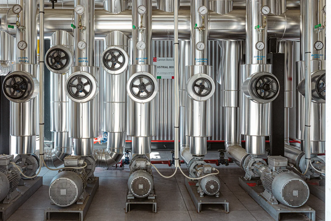 Tubazioni coibentate, valvole e pompe disposte in un locale impianti industriale