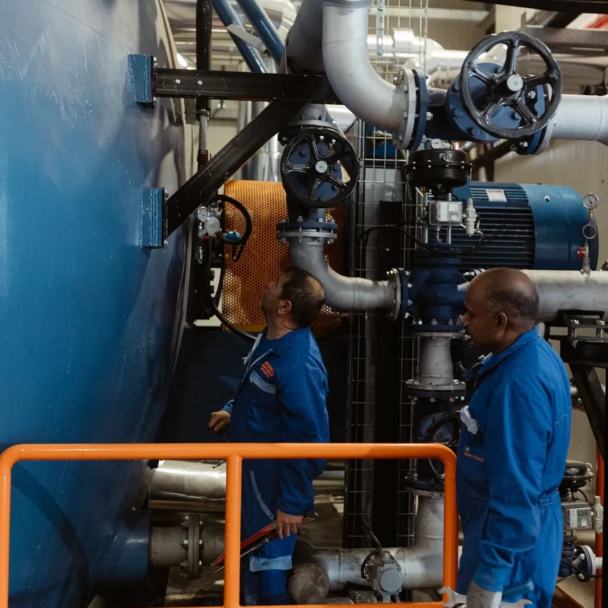 Tecnici vicino al bruciatore e alle tubazioni di un generatore termico industriale